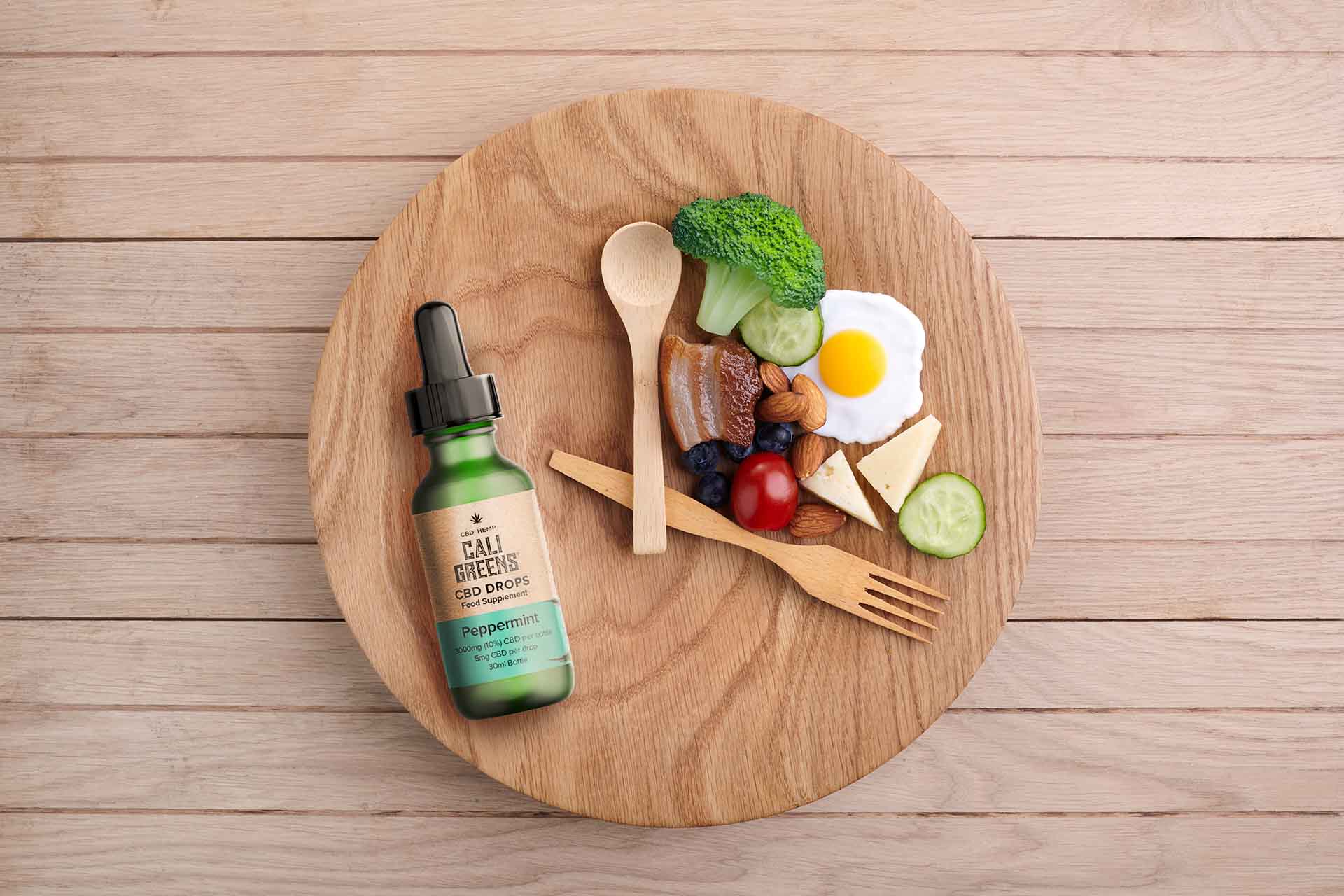 Wooden plate with food and Cali Greens CBD drops with spoons like clock hands (image)