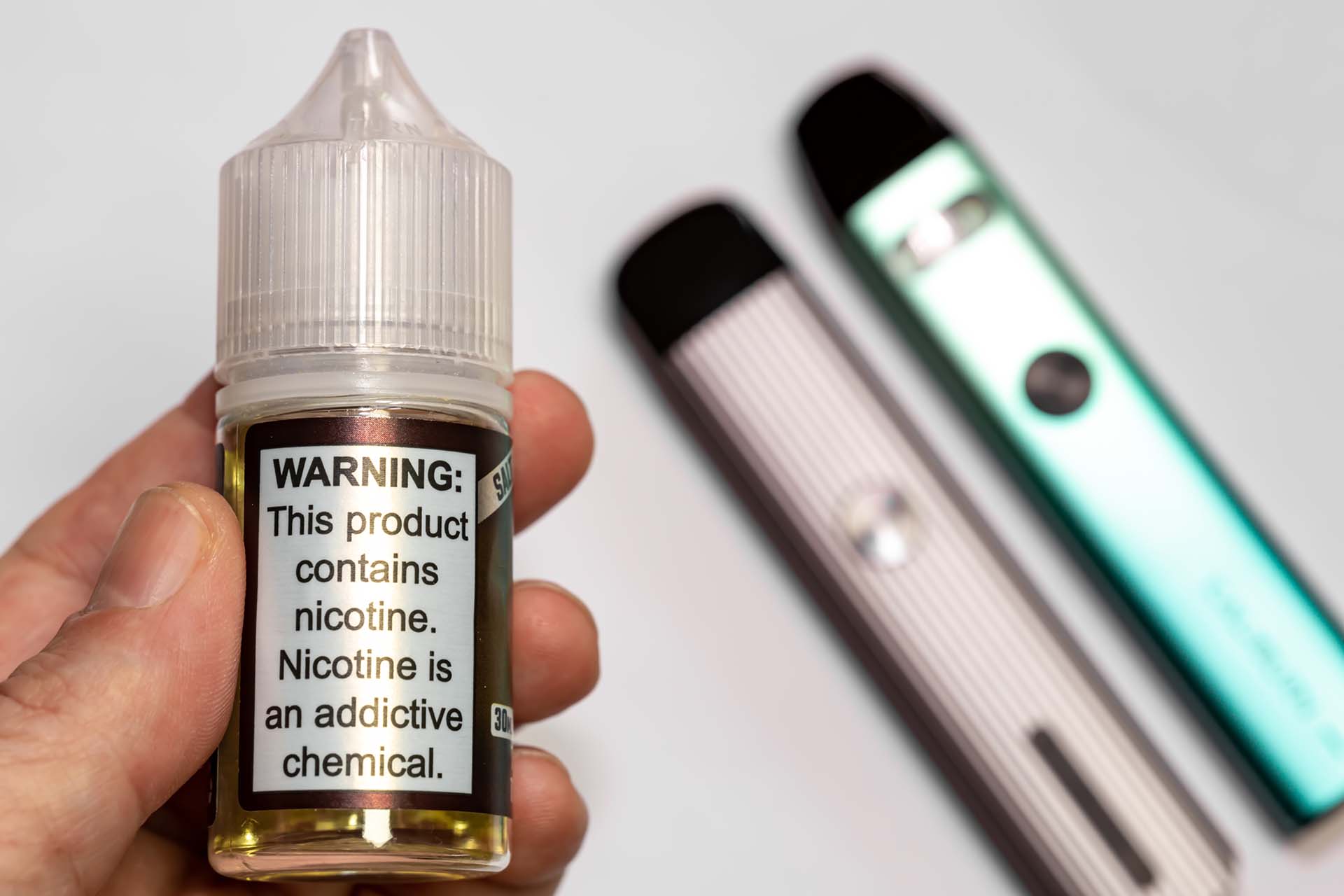 Person holding bottle of vape juice with nicotine warning (Image)