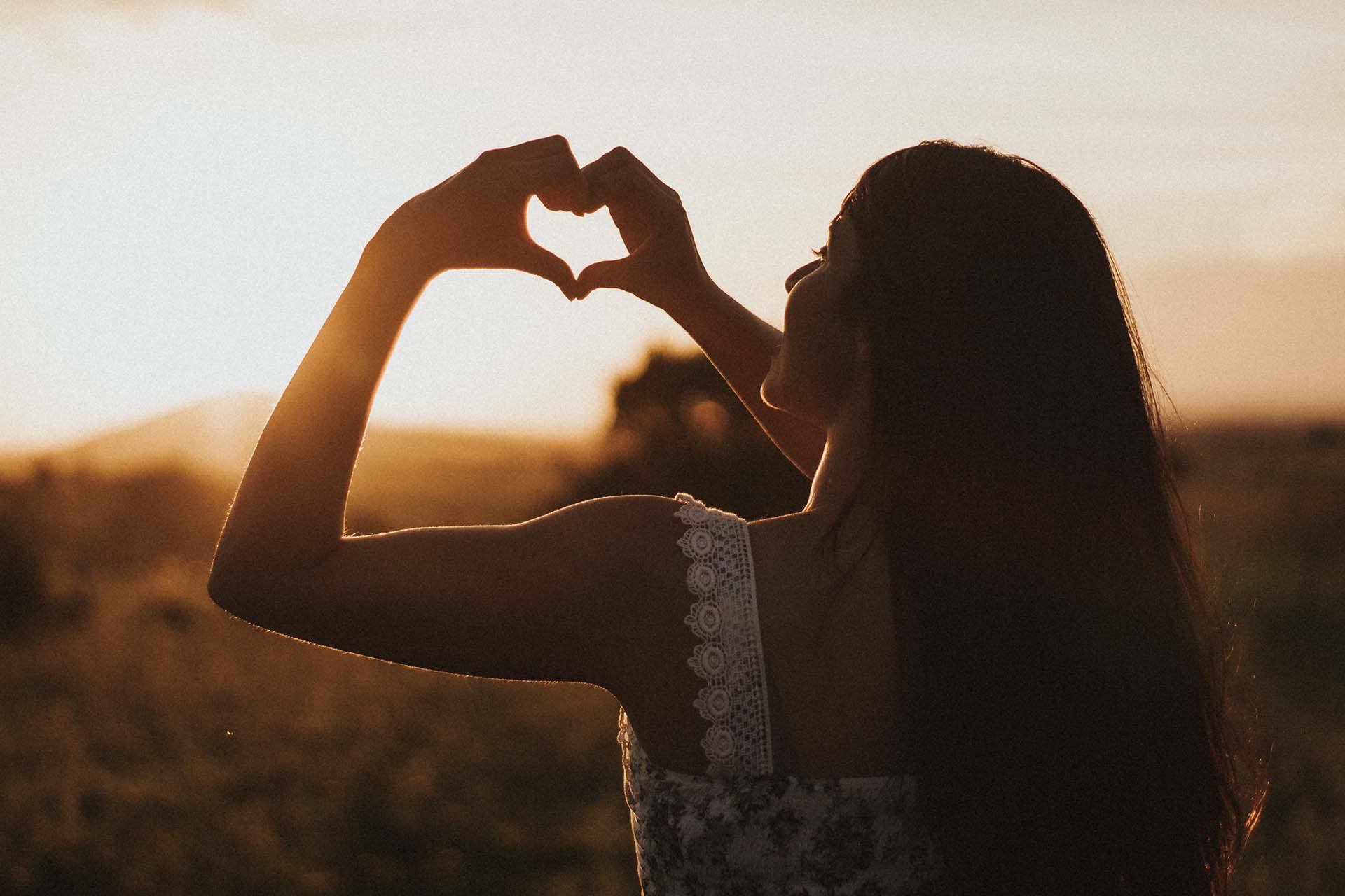 Woman stood by a field making a love symbol with her hands (image)