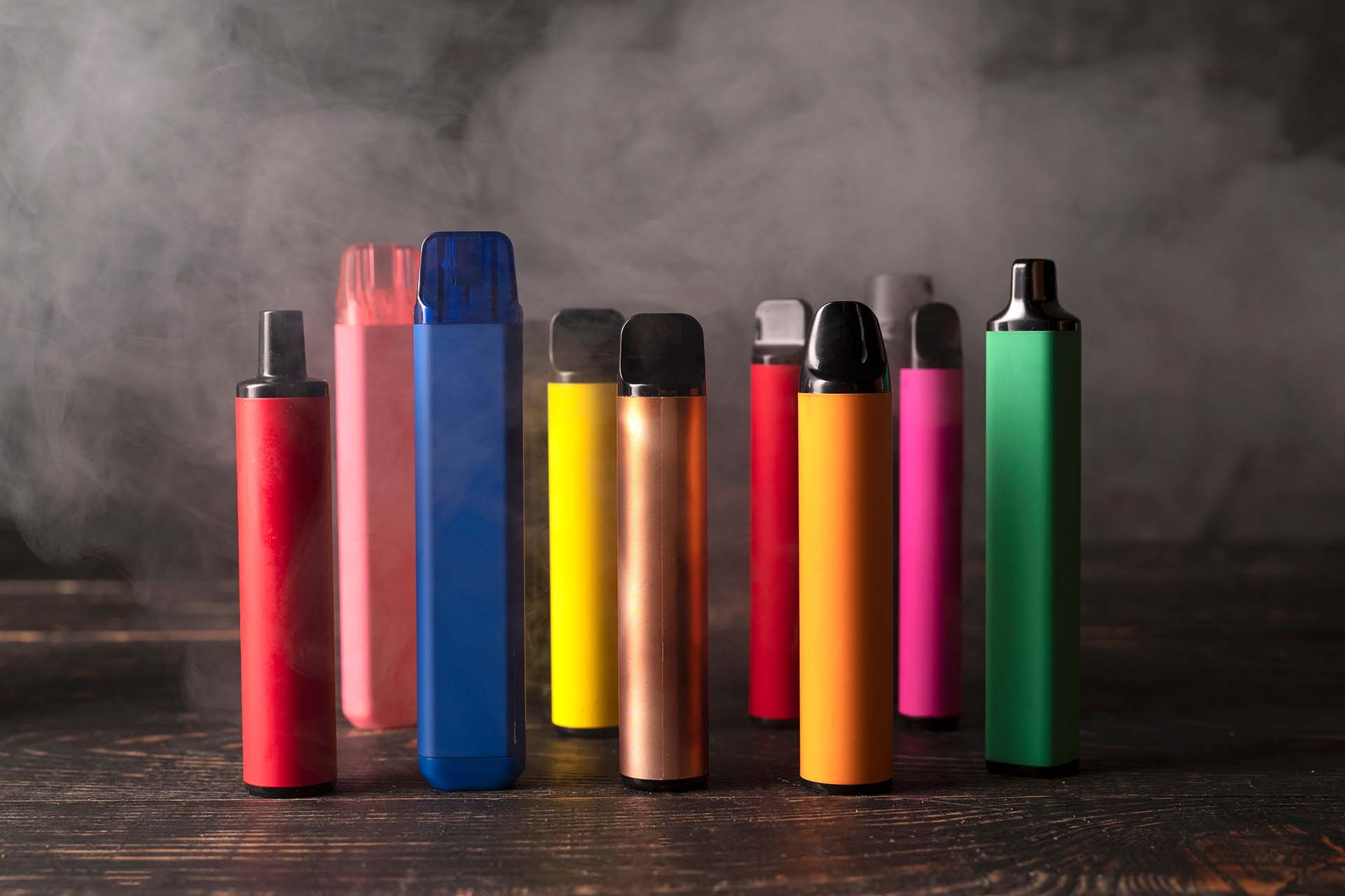 Range of disposable vapes stood up on a dark background surrounded by vapour(Image)